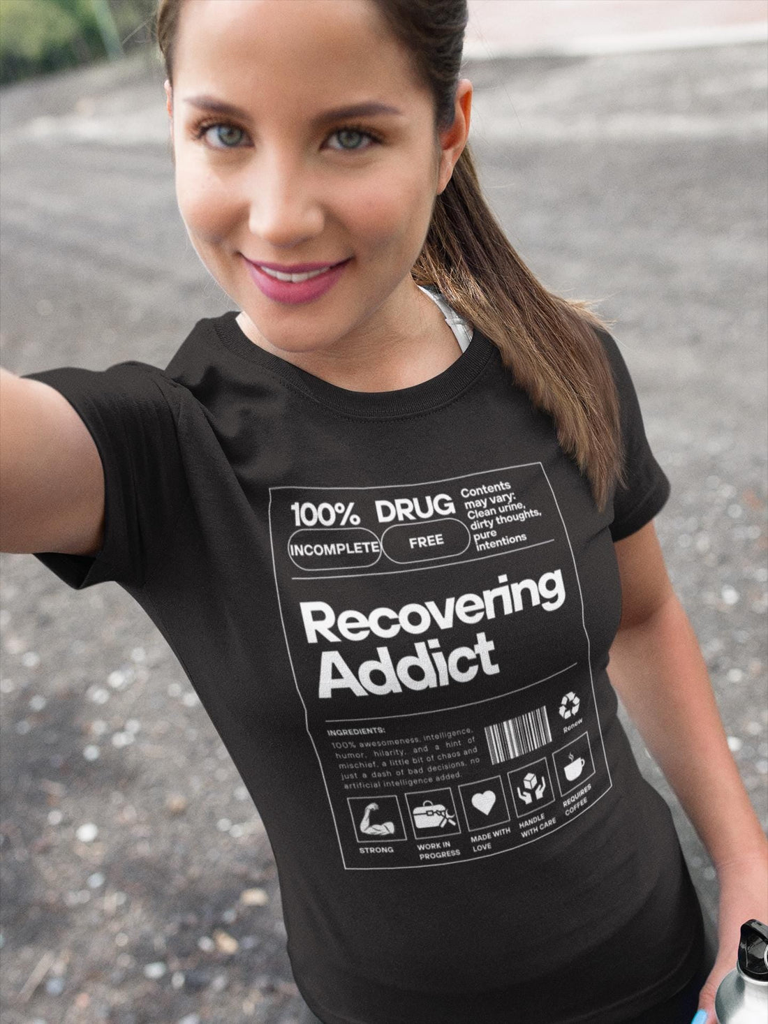Pretty girl taking a selfie wearing a black shirt with "Recovering Addict" printed in white.