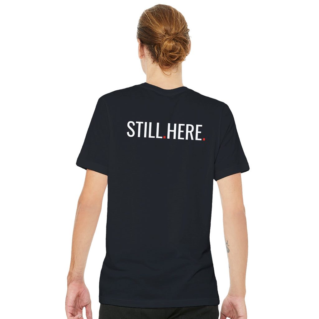 Person wearing a black t-shirt with 'STILL HERE' text on the back, standing against a white background